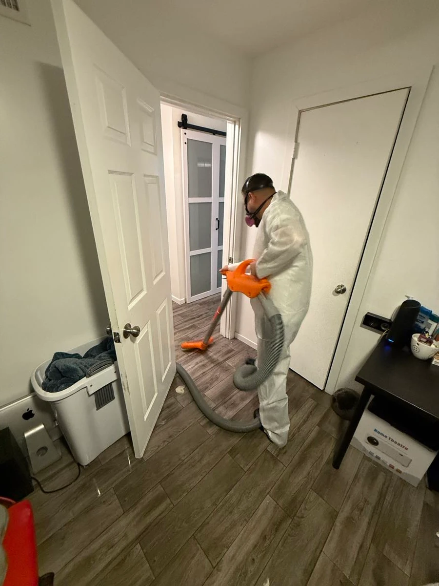 Technician in a protective suit and respirator HEPA-vacuuming a bedroom