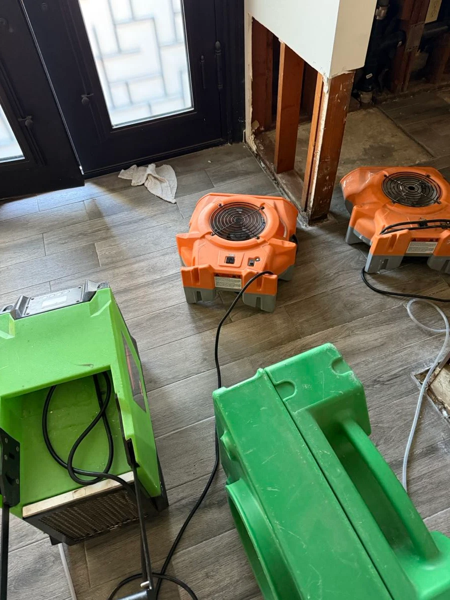 Air movers and a dehumidifier drying a tile floor after water extraction, drywall opened at the base