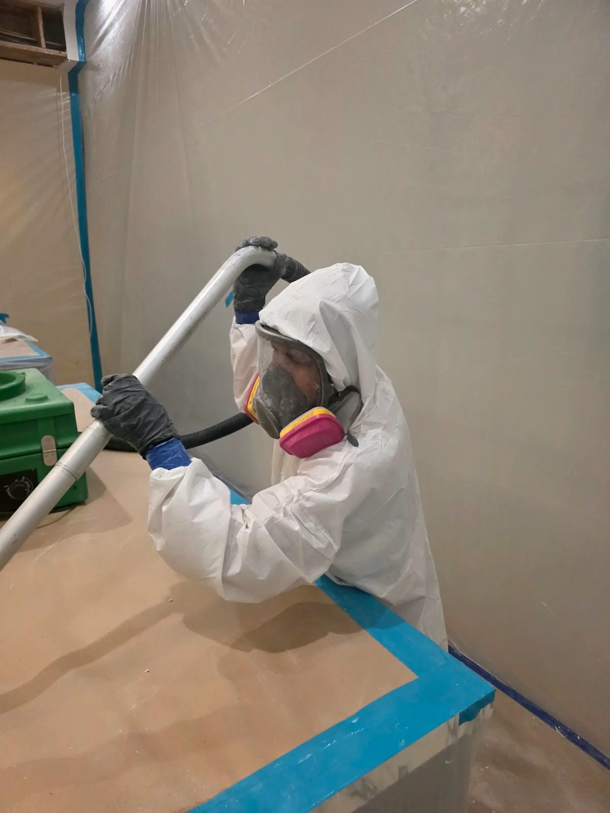Technician wearing a respirator using a vacuum wand inside a protected work area